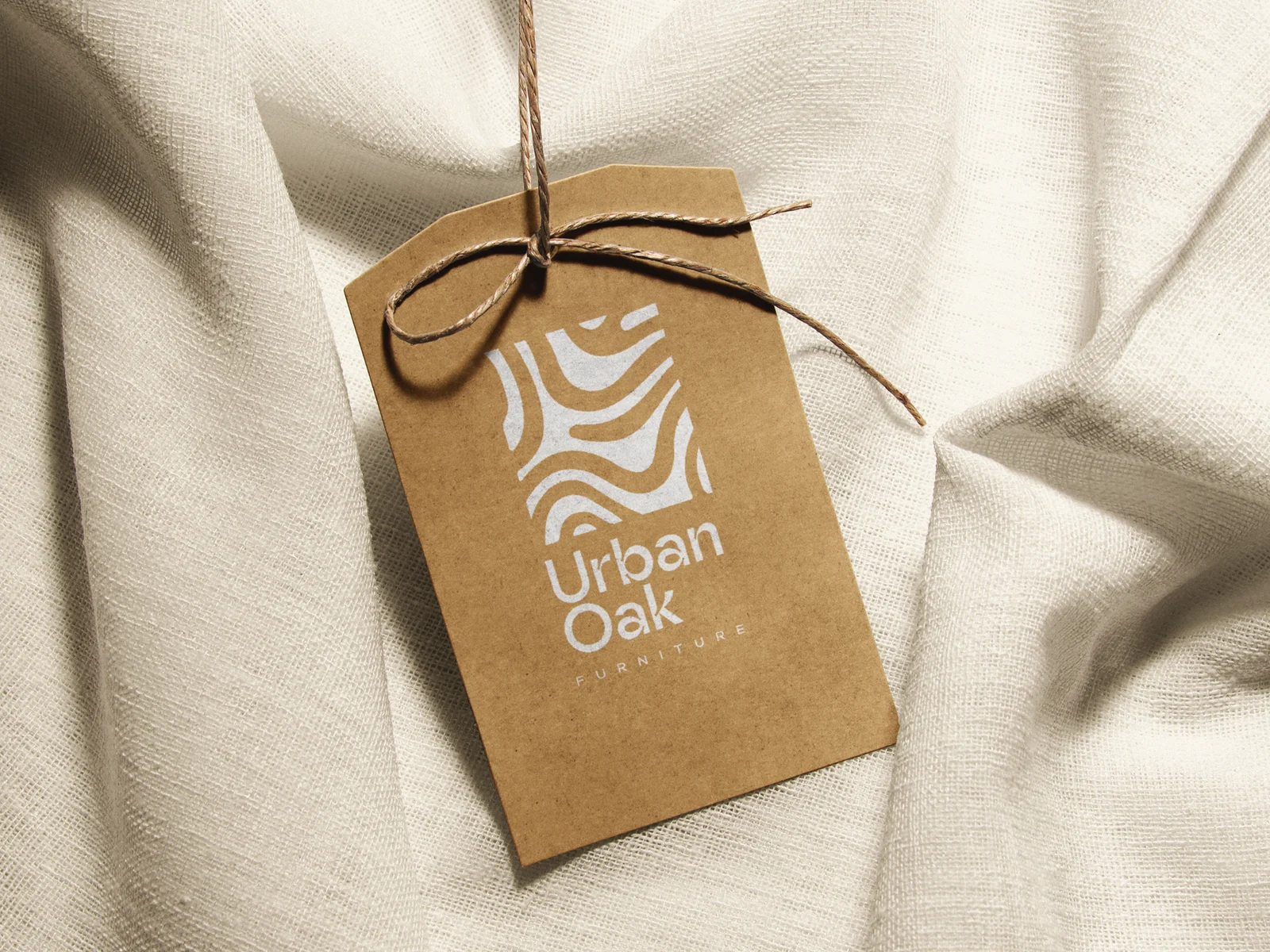 UrbanOak kraft swing tag on natural linen, showing the oak-grain logomark and stacked wordmark